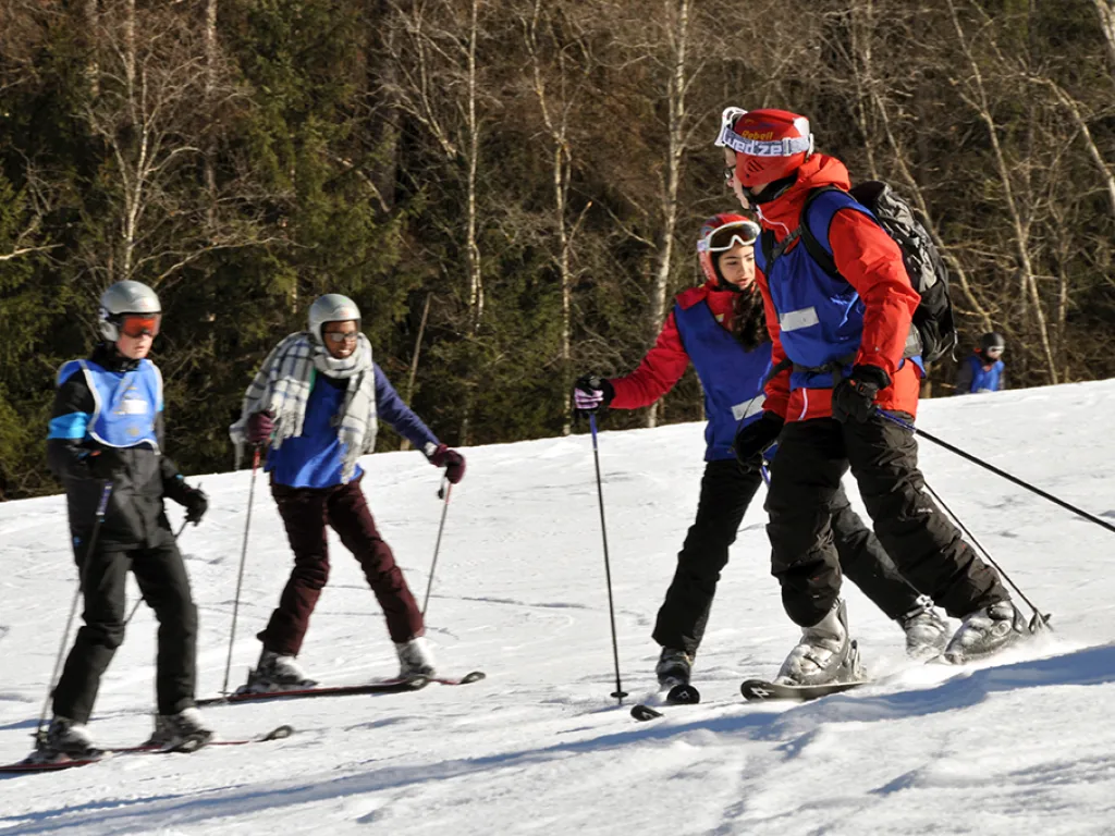 Skifahrende auf der Piste, eine Person in roter Jacke voran.
